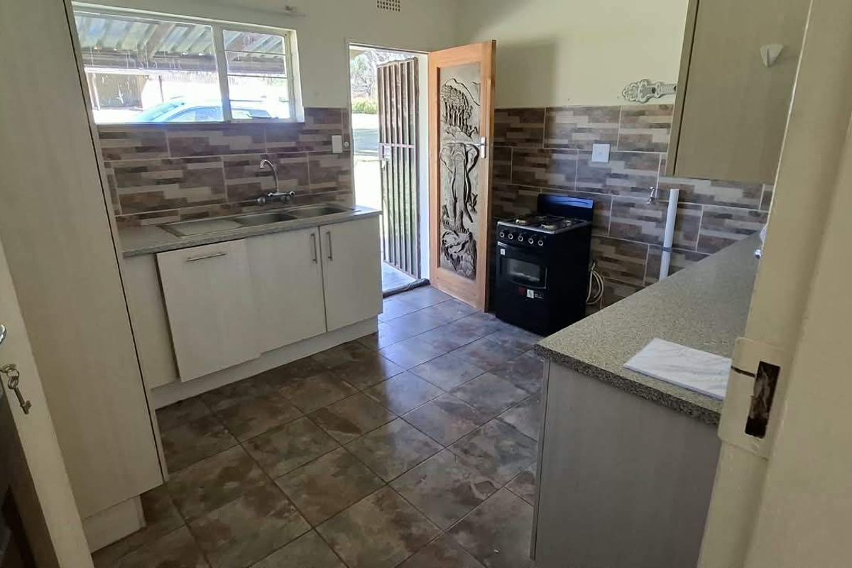 Functional kitchen featuring tiled backsplash, stone-look countertops, double sink, and a freestanding stove with direct access to the exterior.
