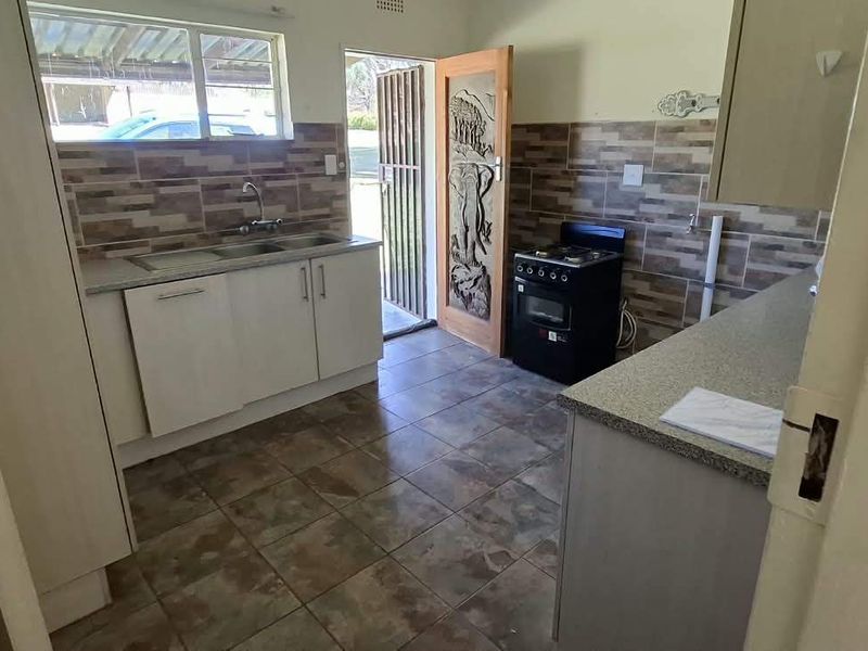 Functional kitchen featuring tiled backsplash, stone-look countertops, double sink, and a freestanding stove with direct access to the exterior.