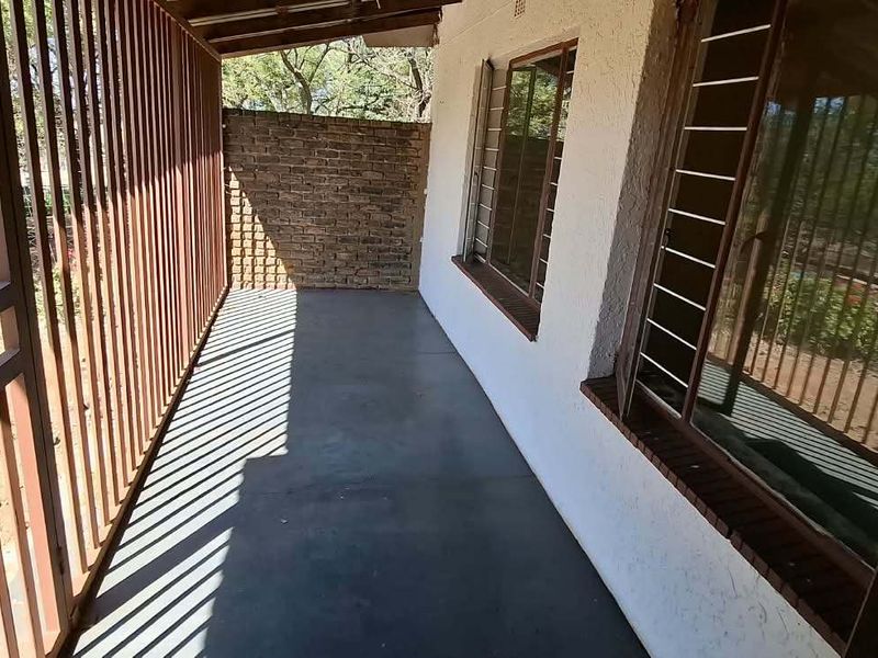 A covered outdoor patio area featuring concrete flooring, exposed brickwork, and security bars on the windows and perimeter.