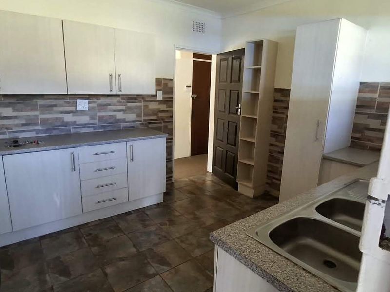 Functional kitchen featuring light-toned cabinetry, tiled backsplash, double stainless steel sink, and gas stove, offering a practical layout for daily meal preparation.