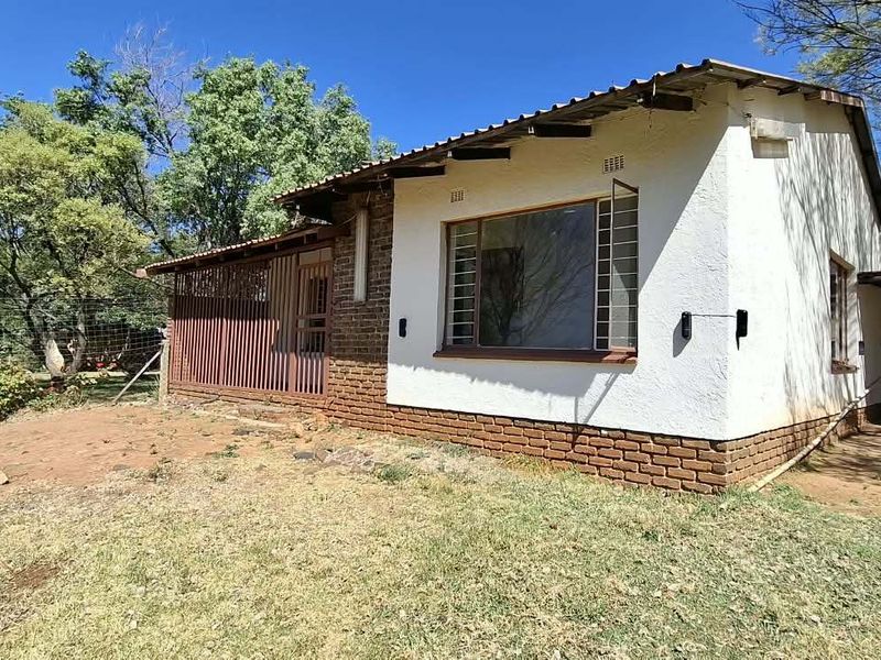 Rear view of a farm-style dwelling featuring a corrugated metal roof, brick and plaster facade, and an attached carport area.