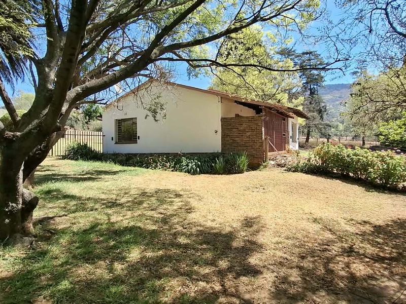 A view of the rear exterior of the farm property, featuring a brick and plaster facade surrounded by mature trees and garden space.