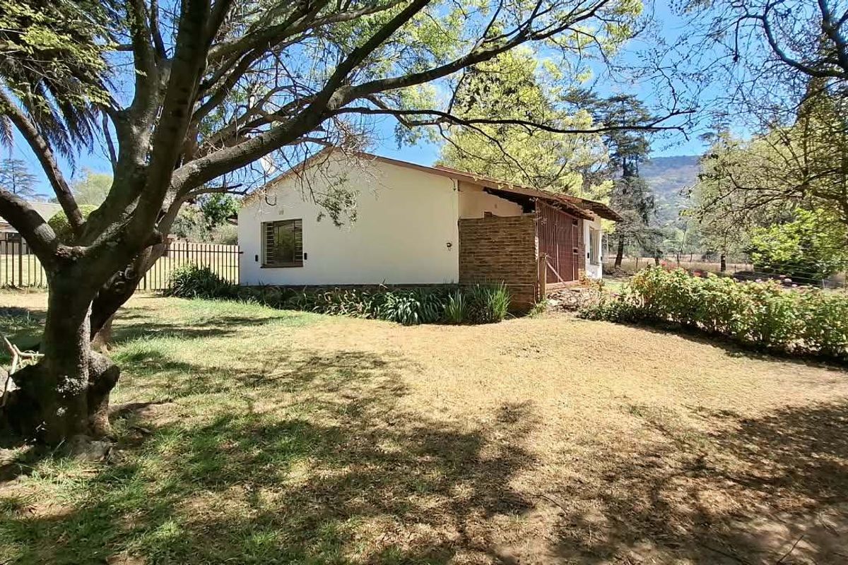 A view of the rear exterior of the farm property, featuring a brick and plaster facade surrounded by mature trees and garden space.
