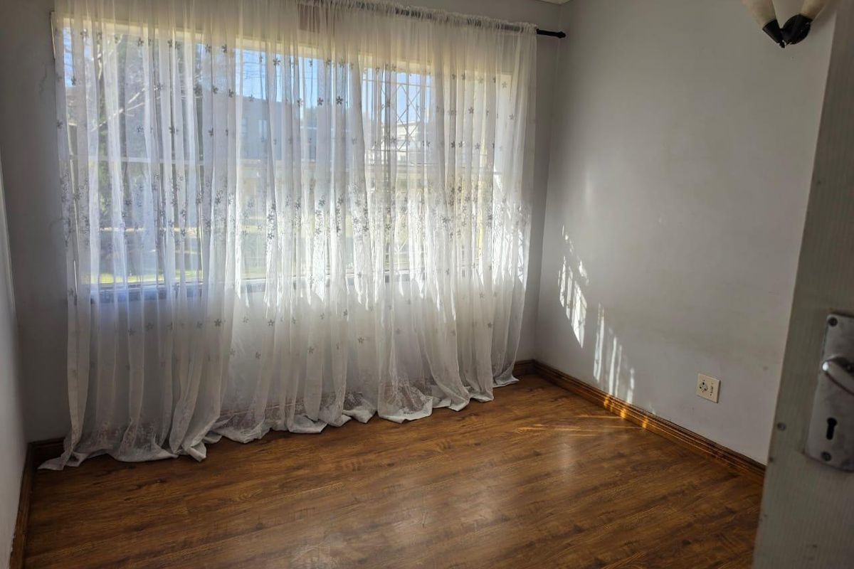 A vacant bedroom featuring laminate flooring, wall-mounted lighting, and a large window fitted with security bars.