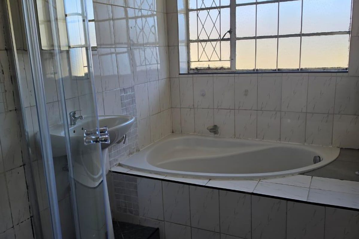 A dated bathroom featuring a built-in bathtub, pedestal basin, and glass shower enclosure with tiled finishes throughout.