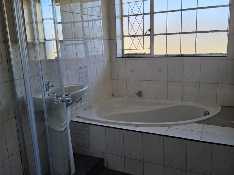 A dated bathroom featuring a built-in bathtub, pedestal basin, and glass shower enclosure with tiled finishes throughout.