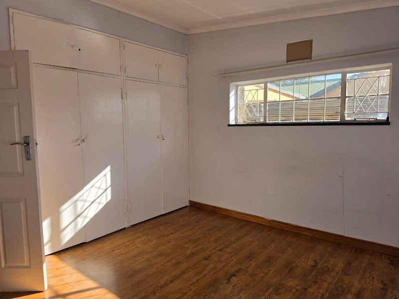 An empty bedroom featuring laminate flooring, built-in cupboards, and a window with security bars, offering a blank canvas for personalization.