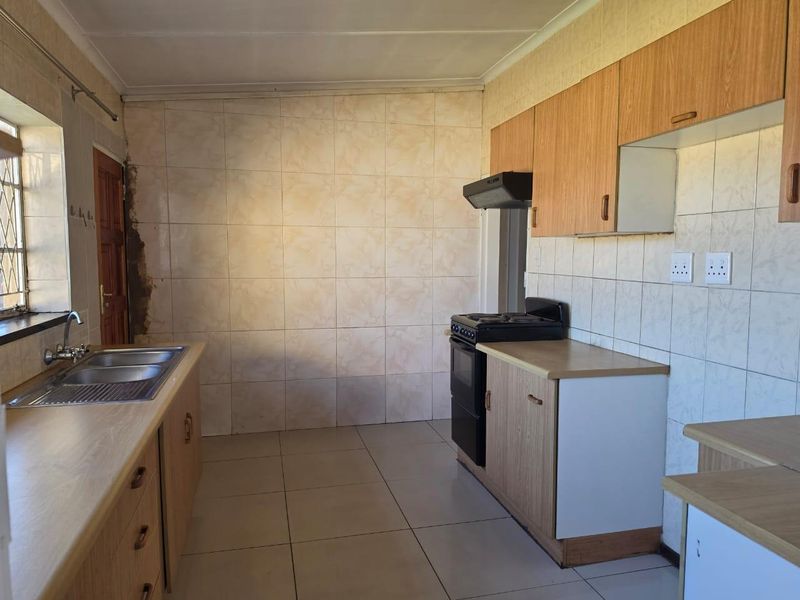 A functional kitchen featuring laminate cabinetry, tiled splashbacks, a stainless steel sink, and a freestanding stove, requiring cosmetic updates to modernize the space.