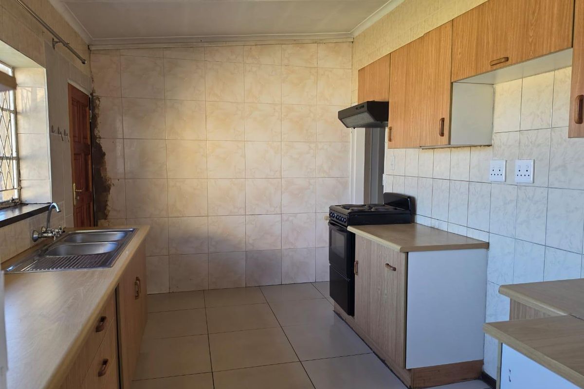 A functional kitchen featuring laminate cabinetry, tiled splashbacks, a stainless steel sink, and a freestanding stove, requiring cosmetic updates to modernize the space.