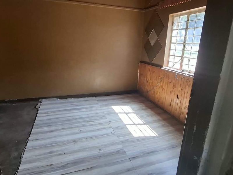 An empty bedroom featuring timber wall paneling, a steel window frame, and partially installed laminate flooring requiring completion.