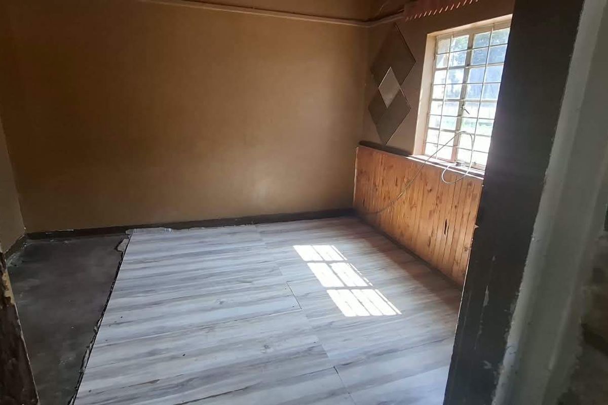 An empty bedroom featuring timber wall paneling, a steel window frame, and partially installed laminate flooring requiring completion.