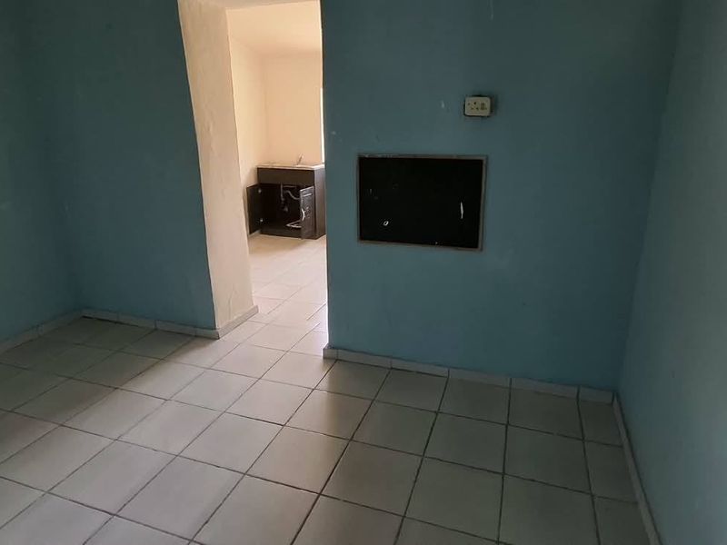 An empty, dated kitchen area featuring tiled flooring and basic built-in cabinetry, requiring cosmetic updates and repairs to wall finishes.