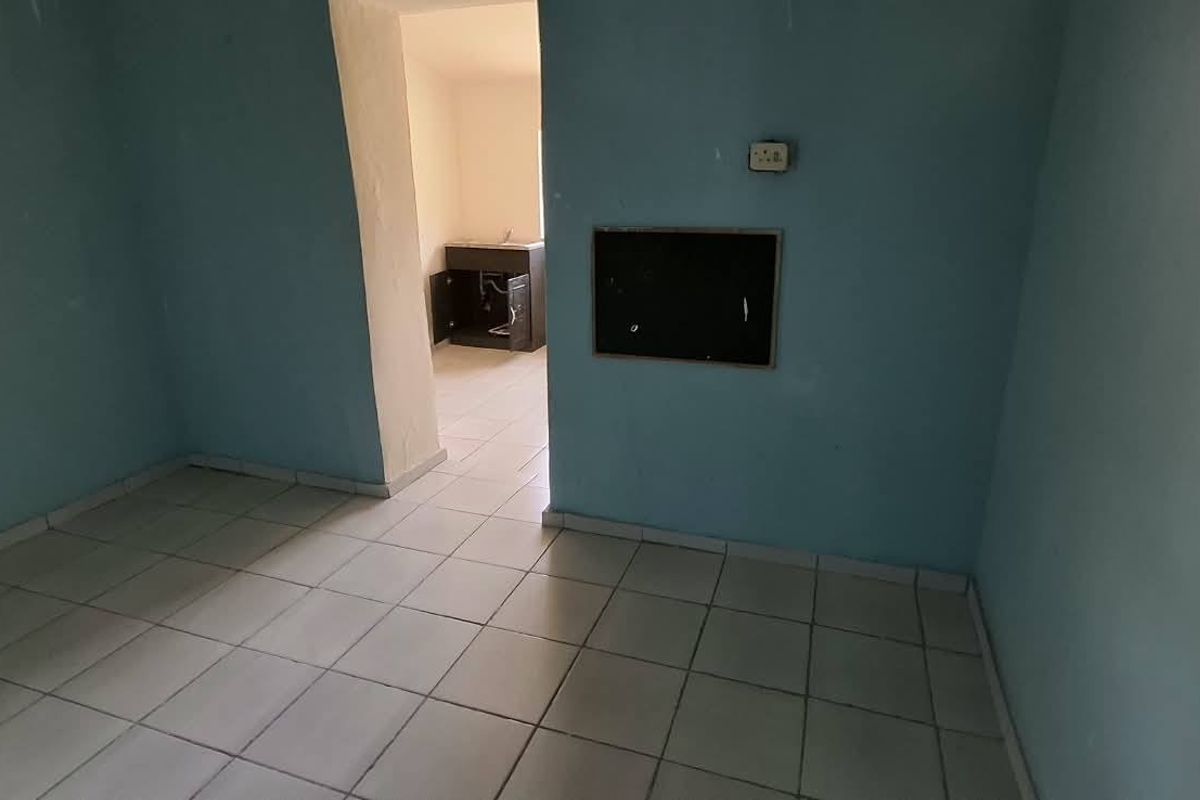 An empty, dated kitchen area featuring tiled flooring and basic built-in cabinetry, requiring cosmetic updates and repairs to wall finishes.