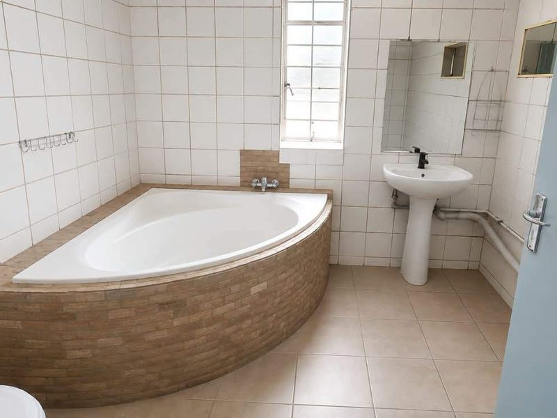 A functional bathroom featuring a corner bathtub, pedestal basin, and neutral ceramic tiling throughout.