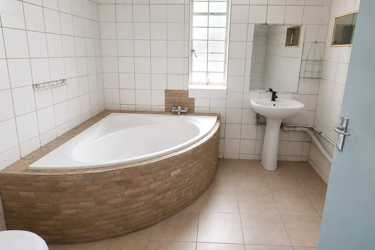 A functional bathroom featuring a corner bathtub, pedestal basin, and neutral ceramic tiling throughout.