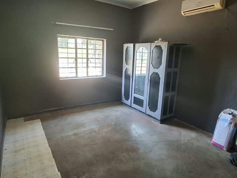 A bedroom featuring dark painted walls, a split-system air conditioner, and security bars on the window, requiring cosmetic updates to improve the overall finish.