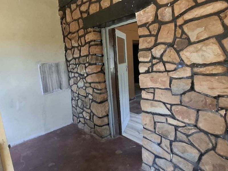 A vacant hallway featuring a rustic stone accent wall and a timber door frame, requiring cosmetic updates and wall repairs.