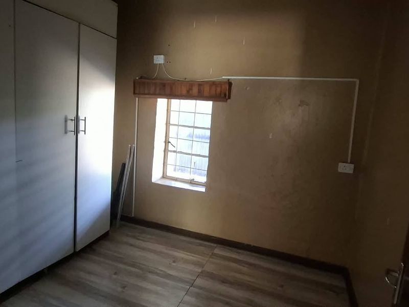 A vacant bedroom featuring built-in cupboards, laminate flooring, and a window with security bars, requiring cosmetic updates to improve its overall condition.