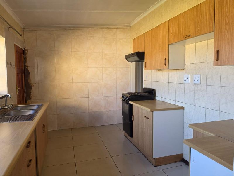 A functional kitchen featuring laminate cabinetry, a double bowl stainless steel sink, a freestanding stove with extractor fan, and tiled finishes throughout.
