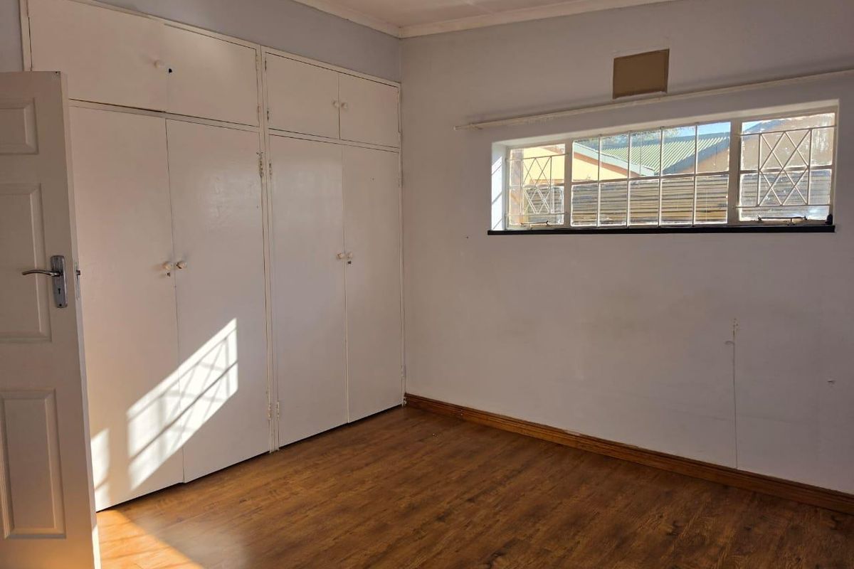 An empty bedroom featuring laminate flooring, built-in cupboards, and a window with security bars, offering a blank canvas for personalization.