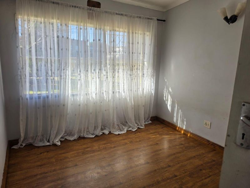 A vacant bedroom featuring laminate flooring, wall-mounted lighting, and a large window fitted with security bars.