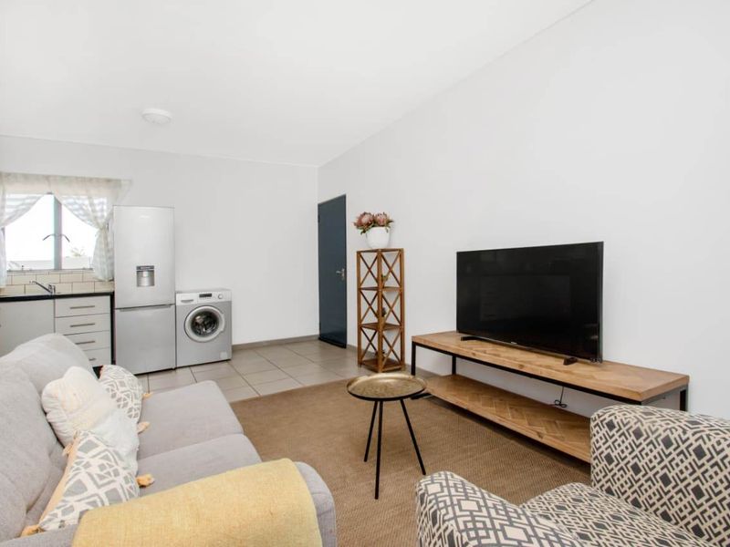 Open plan living area featuring a compact kitchen corner with cabinetry and tiled flooring, seamlessly integrated with the lounge space.