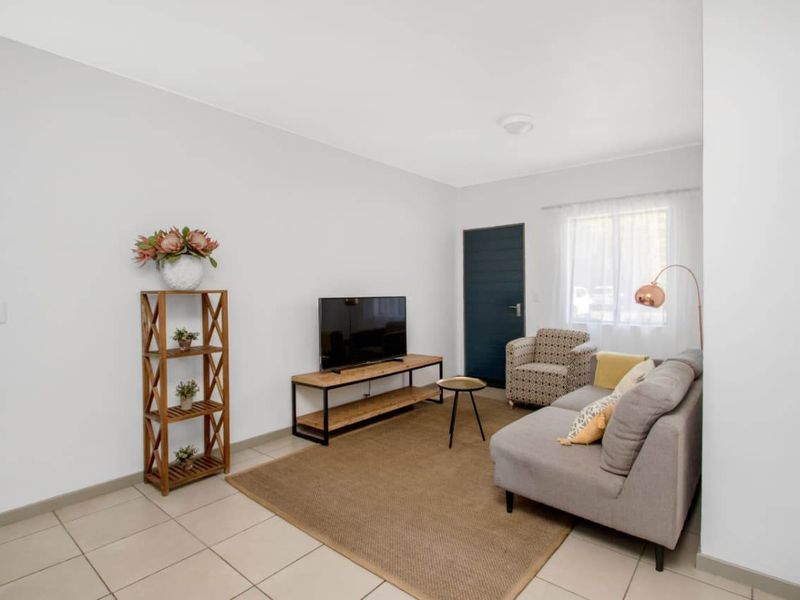 A bright and neutral living room featuring tiled flooring, clean white walls, and natural light from the window.