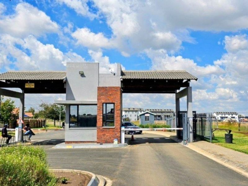 A secure gated entrance to the apartment complex featuring a brick and plaster security gatehouse with an automated boom gate system.
