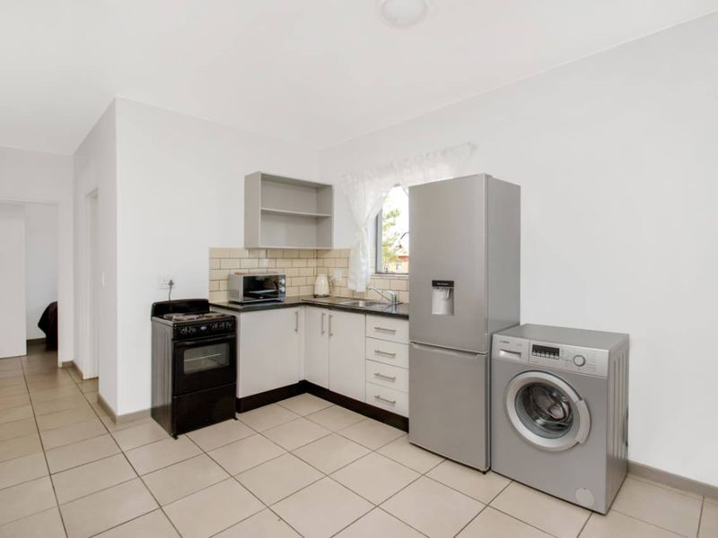 A functional kitchen area featuring tiled flooring, built-in cabinetry with a tiled backsplash, a stainless steel sink, and space for major appliances.