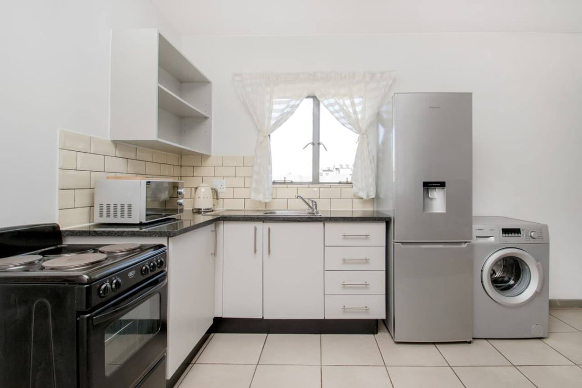 A functional kitchen featuring white cabinetry, subway tile backsplash, dark laminate countertops, and dedicated space for laundry appliances.