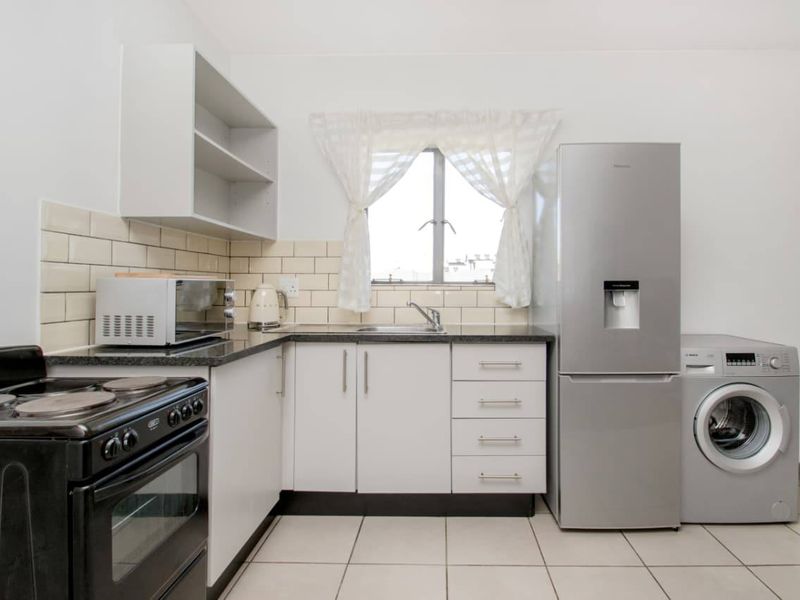 A functional kitchen featuring white cabinetry, subway tile backsplash, dark laminate countertops, and dedicated space for laundry appliances.