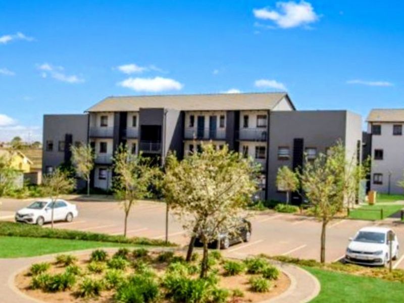 Exterior view of a modern multi-story apartment complex featuring paved parking, landscaped garden areas, and private balconies.