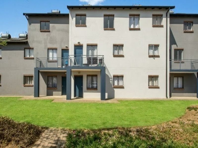 Rear view of a multi-story apartment complex featuring private balconies, solar water heating systems, and a well-maintained communal lawn area.