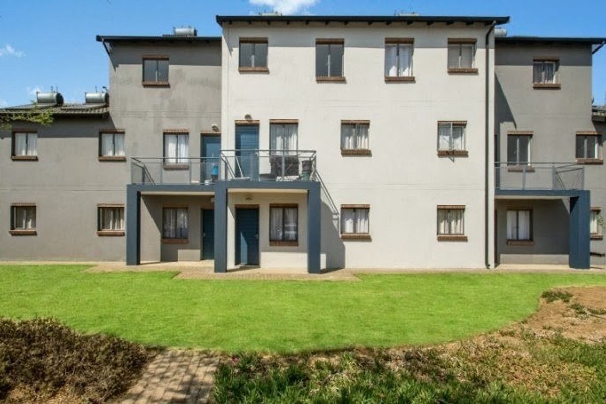 Rear view of a multi-story apartment complex featuring private balconies, solar water heating systems, and a well-maintained communal lawn area.