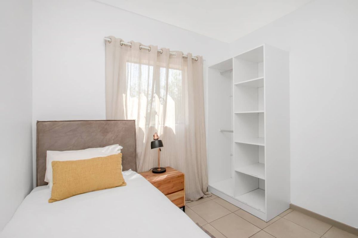 A bright bedroom featuring neutral tiled flooring and a functional built-in white shelving unit for storage.