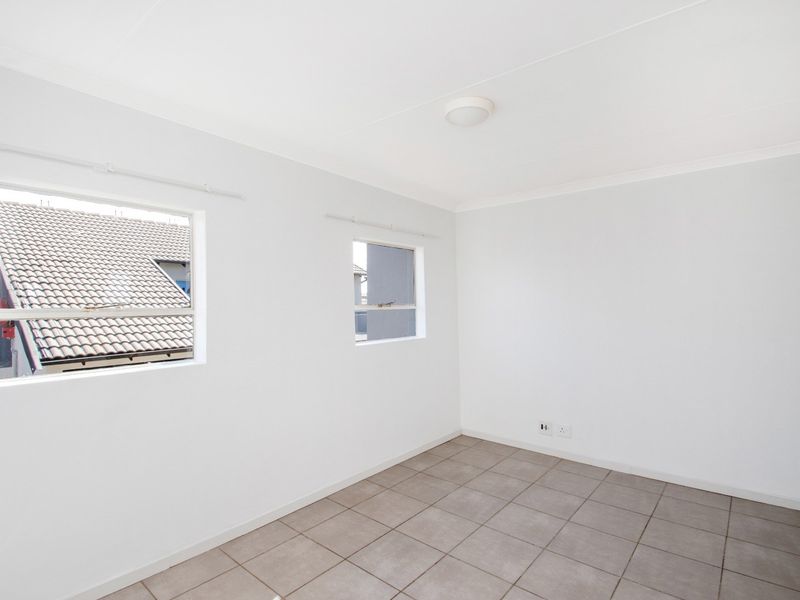 A bright, empty bedroom featuring neutral tiled flooring, clean white walls, and two windows providing natural light.