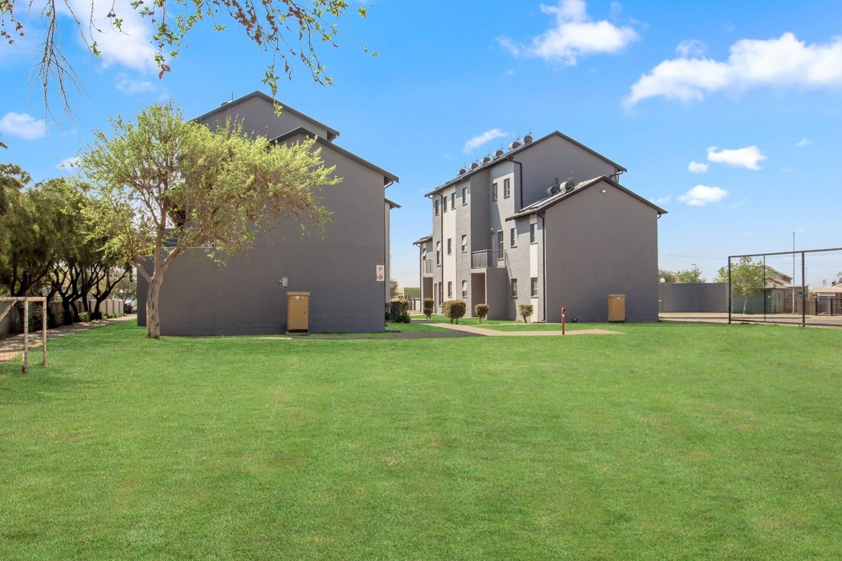 View of the apartment complex exterior featuring well-maintained communal lawns, paved pathways, and solar geyser installations on the roof.