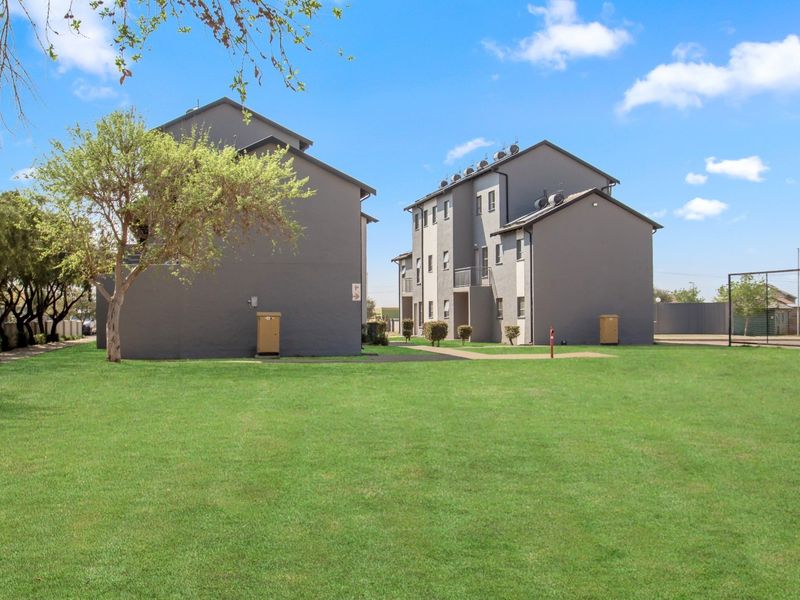 View of the apartment complex exterior featuring well-maintained communal lawns, paved pathways, and solar geyser installations on the roof.
