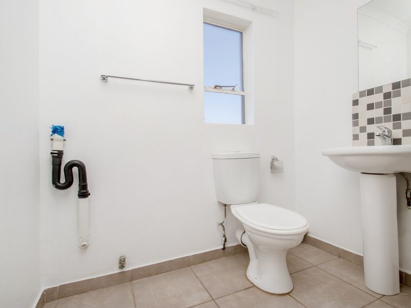 A functional bathroom featuring a pedestal sink, toilet, and tiled flooring, currently requiring minor finishing work on exposed plumbing fixtures.