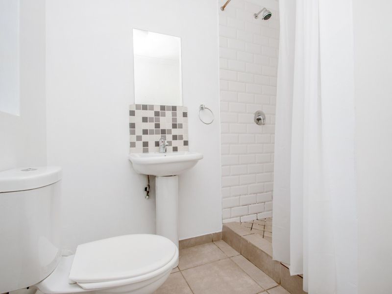 A clean, functional bathroom featuring a pedestal sink, a tiled shower enclosure with a white subway tile finish, and neutral floor tiles.
