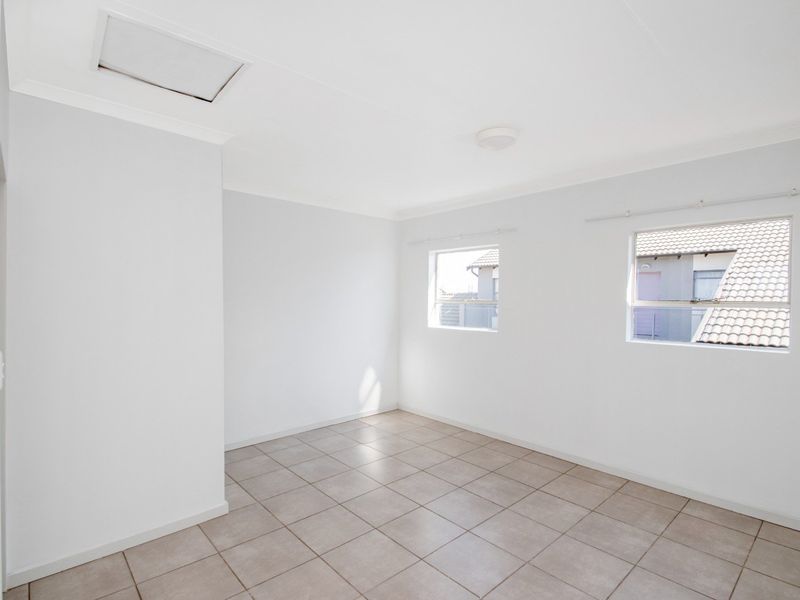 A bright, empty bedroom featuring neutral tiled flooring, clean white walls, and two windows providing natural light.