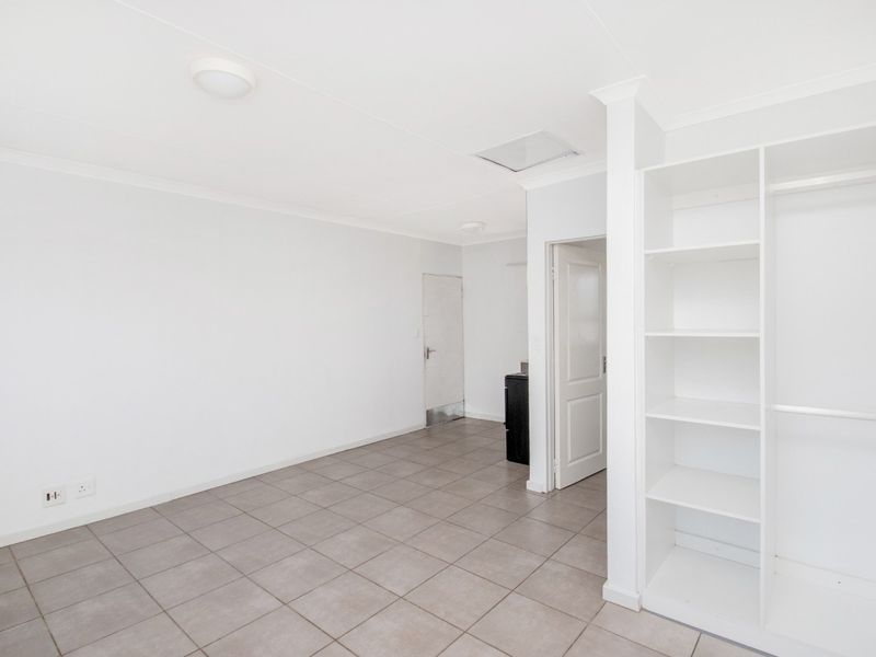 A bright, empty bedroom featuring neutral tiled flooring and convenient built-in shelving units, offering a clean and versatile space.