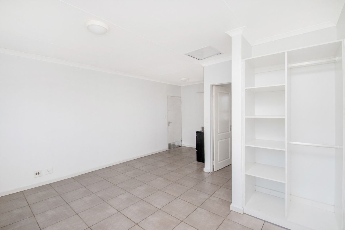 A bright, empty bedroom featuring neutral tiled flooring and convenient built-in shelving units, offering a clean and versatile space.
