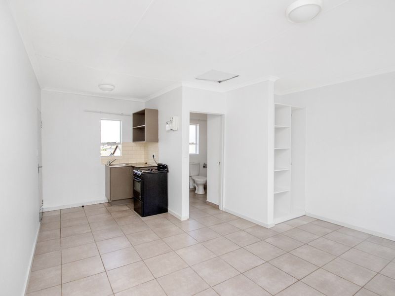 Open plan living area featuring tiled floors, a compact kitchen with built-in cabinetry, and an adjacent bathroom entrance.