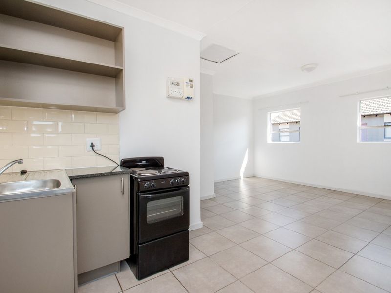 An open-plan kitchen and living area featuring neutral tiled flooring, built-in cabinetry, and a functional kitchen layout with a stove and subway tile backsplash.