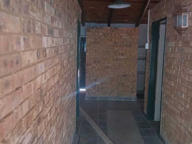 A rustic hallway featuring exposed brick walls, tiled flooring, and a timber beam ceiling, providing a characterful transition between rooms.