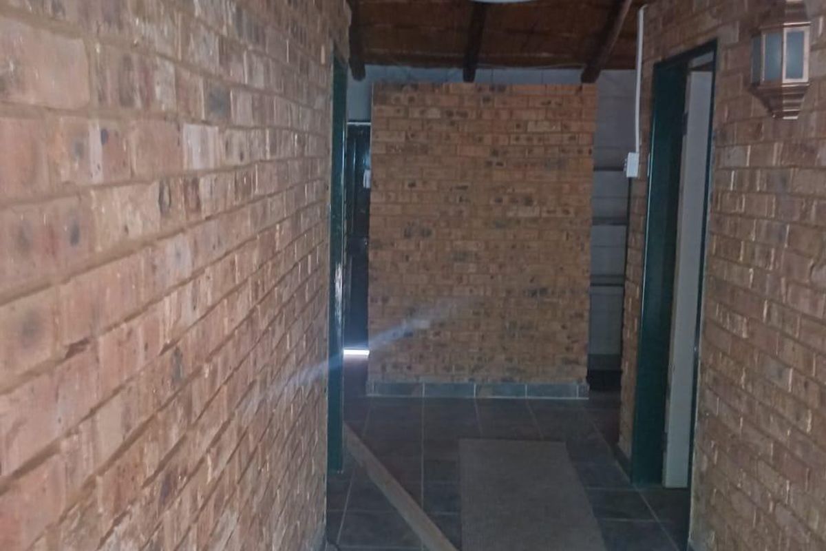 A rustic hallway featuring exposed brick walls, tiled flooring, and a timber beam ceiling, providing a characterful transition between rooms.