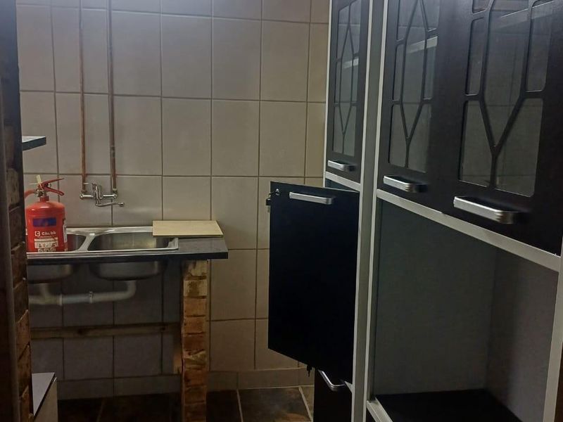 A functional scullery area featuring a double basin sink, tiled splashback, and built-in storage cabinetry with exposed copper plumbing details.