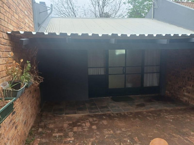 A covered outdoor patio area featuring a corrugated metal roof, exposed timber beams, and tiled flooring, providing a functional space for outdoor living.
