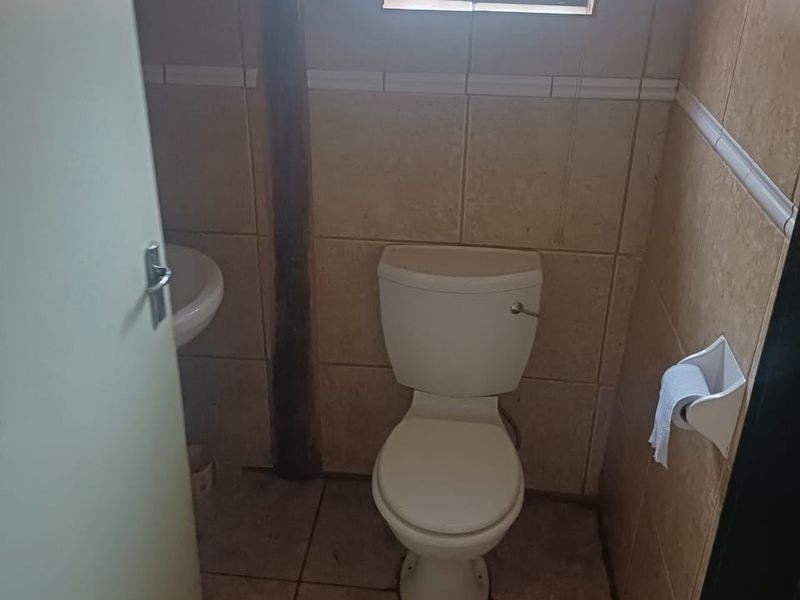 A compact guest bathroom featuring a standard toilet, wall-mounted basin, and tiled finishes, requiring cosmetic updates to improve its overall condition.